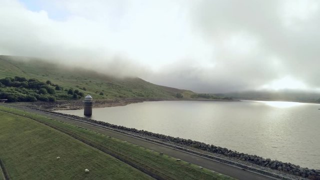 Aerial view, backward move. Drone panorama of Llyn Celyn water reservoir with dam and sheep on grass in Wales