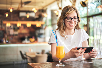 Woman texting and listening music on the mobile phone in the cafe