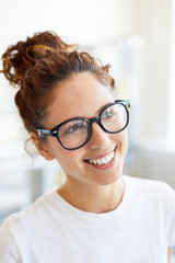 Cheerful young female office manager with toothy smile looking straight during work