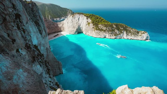 4k Timelapse of the world famous Navagio beach, Zakynthos, Greece. Turquoise sea water rolled to white sand beach with Shipwreck. Clouds shadow moving on water. Fist tourist boats arrived the bay
