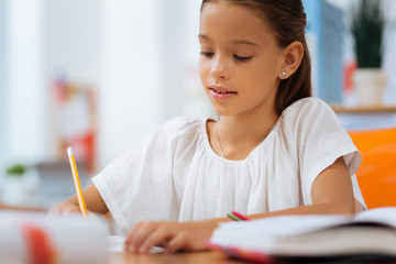 School time. Concentrated schoolgirl sitting in a room while doing an exercise