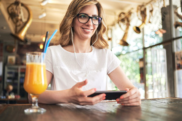 Woman texting and listening music on the mobile phone in the cafe