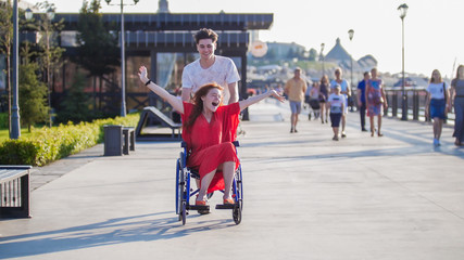 Guy rolls a happy disabled girl in a wheelchair on the waterfront