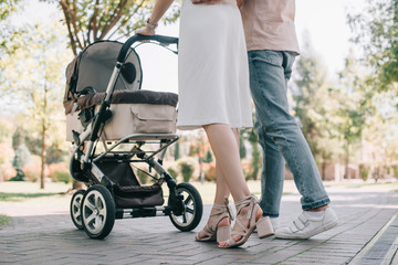 cropped image of parents walking with baby carriage in park