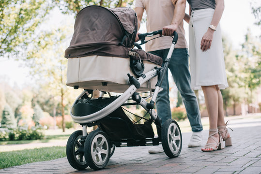 cropped image of mother and father walking with baby carriage in park