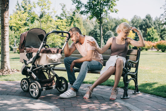 aggressive parents sitting on bench near baby carriage in park