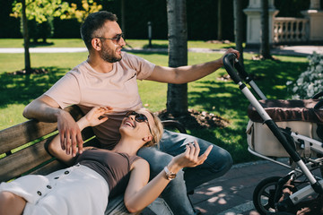 wife lying on husband legs near baby carriage in park