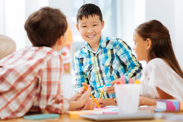 Colors. Cheerful boy drawing while spending time with classmates