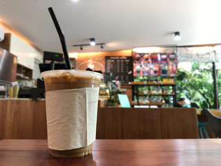 Cold brew coffee or chocolate in plastic cup on rustic table with blurred background