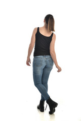 full length portrait of brunette girl wearing black single and jeans. standing pose with back to the camera. isolated on white studio background.