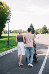 Fototapeta premium rear view of parents walking with baby carriage on road in park