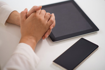 Close-up of clasped hands on table with pc tablet and smartphone. Caucasian businesswoman sitting table with digital devices. Wireless technology