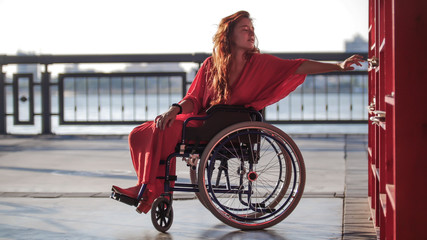 Beautiful red-haired girl in a wheelchair trying to reach a book on a bookshelf