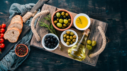 A set of olives, olive oil, bread, cheese and spices. On a black wooden background. Free space for...
