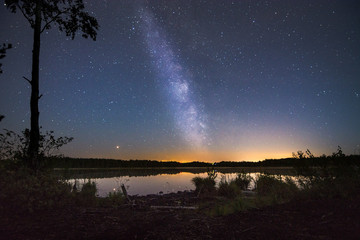 Glowing milky way over a still lake with sunset in the background. Tropical summer nights with million stars above and colorful sky. 