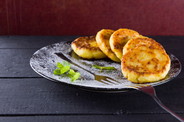 Cottage cheese pancakes on a dark background. Syrniki with fresh mint. Pancakes with cottage cheese on a black plate sprinkled with powdered sugar. Healthy food