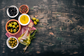 A set of olives and olive oil and rosemary. Green olives and black olives. On a black wooden background. Free space for text.