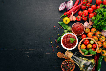 Traditional tomato ketchup sauce. Cherry tomatoes, spices, chili peppers, olive oil, parsley. Top view. On a black wooden background. Free space.