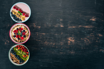 Oatmeal with yogurt, fruits and berries in plates. Breakfast. On a black wooden background. Top view. Free space for text.