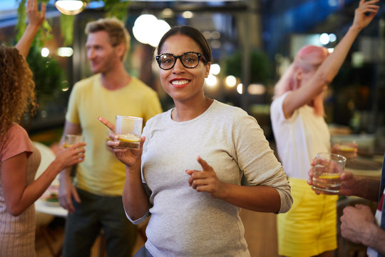 Young cheerful woman in casualwear having drink and enjoying dance among her friends