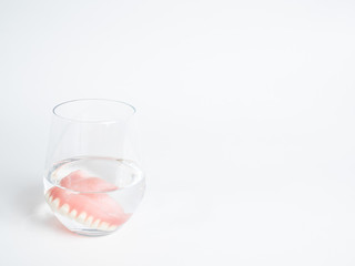A denture in a glass of water on white background, perfect picture for appointment cards