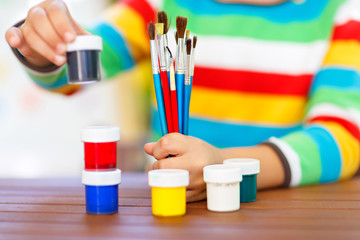 Fototapeta premium Close-up of hands of kid holding watercolors and brushes. child and student is back to school. Education, school, learning concept. School, preschool nursery equipment.