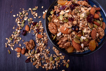 Granola made of cereals, nuts and seeds in a bowl and scattered around the dark table