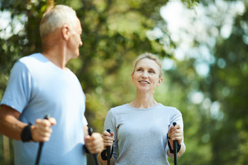 Sporty aged female and her husband trekking in park or forest on summer weekend