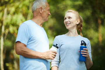 Healthy mature man and woman in activewear having refreshment after workout in natural environment