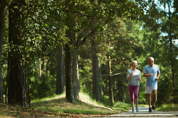 Healthy active senior couple in sportswear running among green trees on sunny day in summer