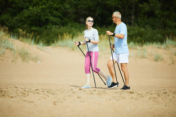 Mature man and woman in activewear talking while trekking on sandy beach