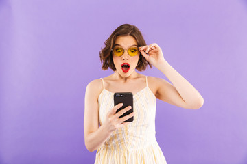 Shocked young woman using mobile phone isolated over purple wall background.