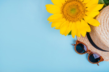 Fashion flatlay with sunglasses, straw boater hat and bright big yellow sunflower on blue background. Flatlay style.