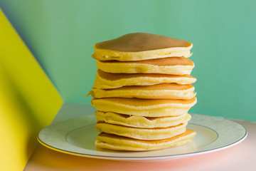 Pancakes on a yellow green background. Many pancakes on a white plate with copy space. Delicious dish for breakfast in the style of pop art. Festive food on a colorful background. French breakfast