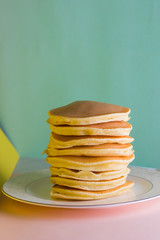 Pancakes on a yellow green background. Many pancakes on a white plate with copy space. Delicious dish for breakfast in the style of pop art. Festive food on a colorful background. French breakfast