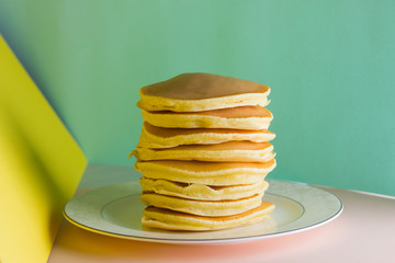 Pancakes on a yellow green background. Many pancakes on a white plate with copy space. Delicious dish for breakfast in the style of pop art. Festive food on a colorful background. French breakfast