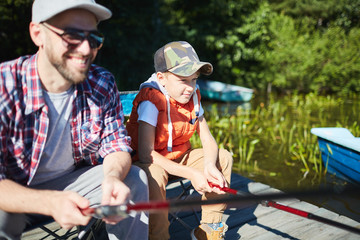 Satisfied boy sitting on fishing together with his father in sunny summer day