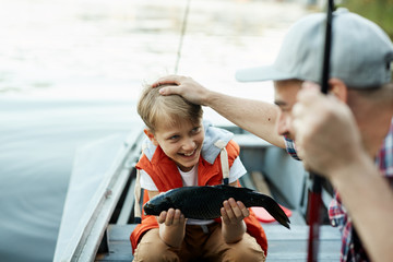Happy boy holding big fish, and showing it to his father, while they are on the boat © pressmaster