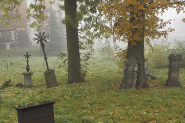opuszczony stary cmentarz w jesienny mglisty poranek, pochylone krzyże i nagrobki w otoczeniu jesiennych drzew