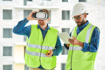 Waist up portrait of two contemporary workers using VR to visualize projects on construction site