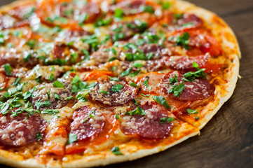 sliced Pepperoni Pizza with Mozzarella cheese, salami, Tomatoes, pepper, Spices and Fresh Basil. Italian pizza on wooden background
