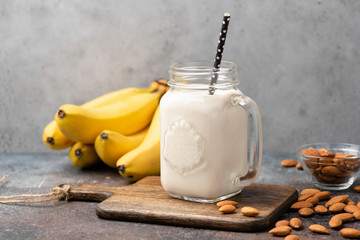 Banana protein smoothie in drinking glass on wooden serving board