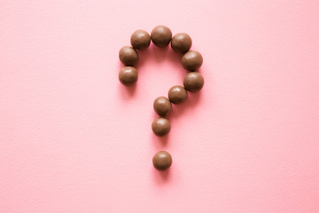Question mark created from chocolate balls on the pastel pink table. Choice of the best sort and...