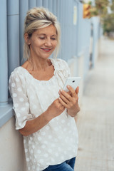 ältere, elegante frau schaut auf ihr mobiltelefon und lächelt