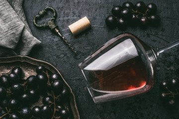 Red wine concept with glass, grapes and vintage corkscrew on dark background, top view