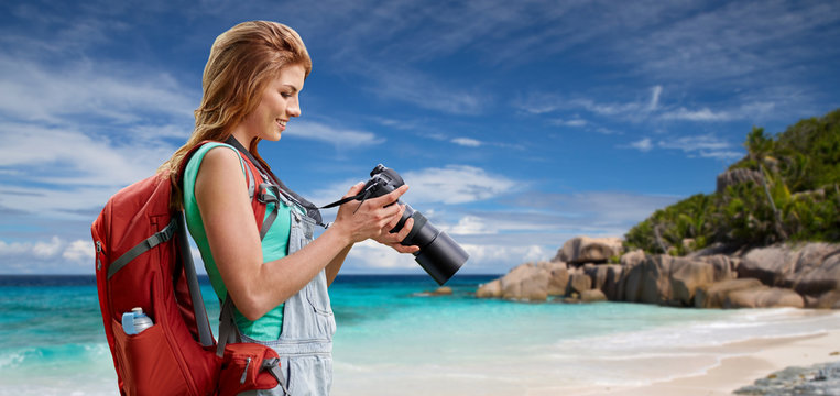 travel, tourism and photography concept - happy young woman with backpack and camera over background of seychelles island beach in indian ocean