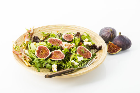 gemischter Blattsalat mit Feigen, Tomaten, Schafskaese und Crossinis mit Schinken auf Holzteller, Freisteller