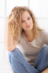 Naklejka premium portrait of young woman caressing her long hair, sitting on floor dressed in jeans and T shirt, isolared on white