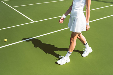 cropped shot of female tennis player in white sportswear walking on tennis court
