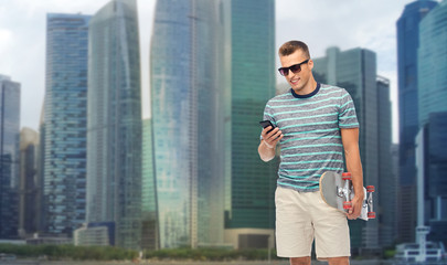 technology, leisure and skateboarding concept - smiling young man with skateboard and smartphone over singapore city skyscrapers background